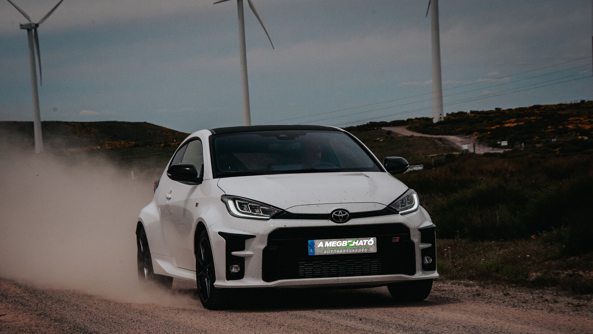 Fehér Toyota a szélerőművek előtt